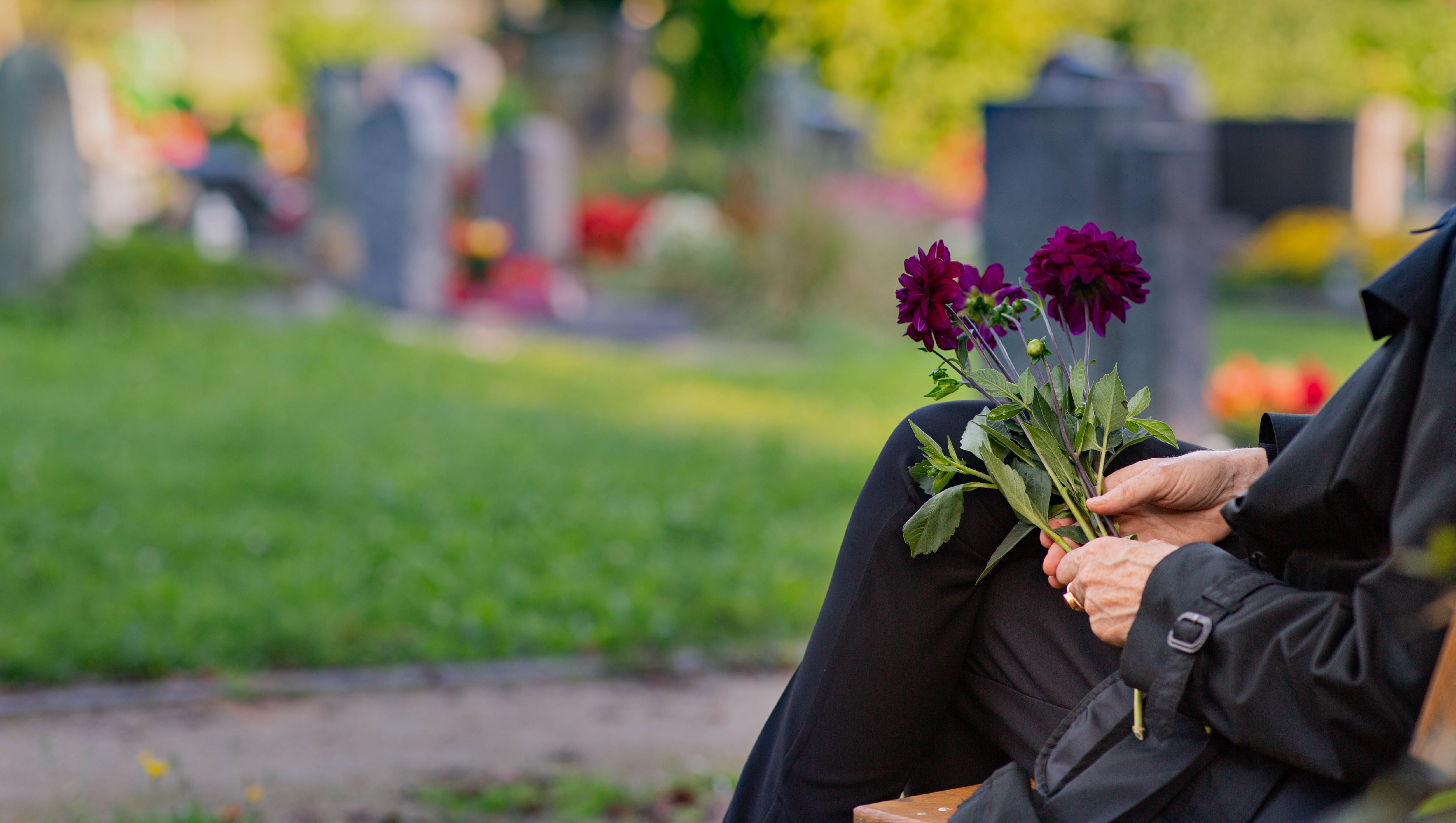 Sitzende Frau mit Blumen in der Hand auf einem Friedhof; Foto: Fundus